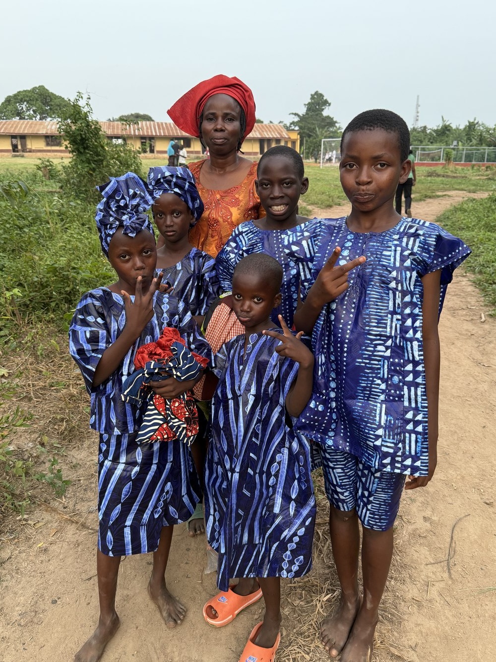 Onipe family in traditional adire dress on the school grounds, completed school building visible behind